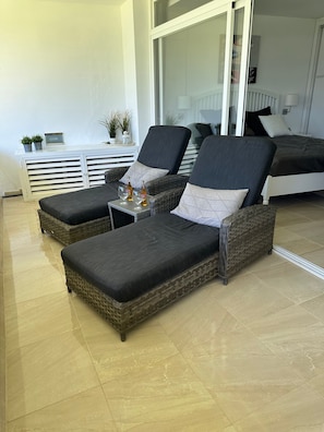 Un balcon avec deux fauteuils de relaxation en osier, une petite table avec des boissons et une console blanche agrémentée de plantes.