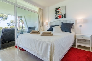 Una camera da letto con un letto, un comodino, una sedia, una finestra con tende e un quadro appeso al muro.