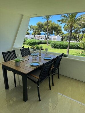 Zona pranzo con tavolo imbandito per quattro persone, sedie, una pianta in vaso e vista sul mare e sugli edifici.