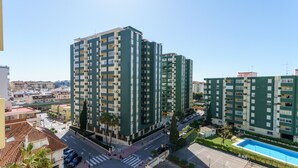 Un edificio residencial alto con balcones, una piscina y un paso de peatones al frente.