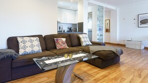 Una sala de estar moderna con un sofá, una mesa de centro de vidrio y una cocina al fondo.