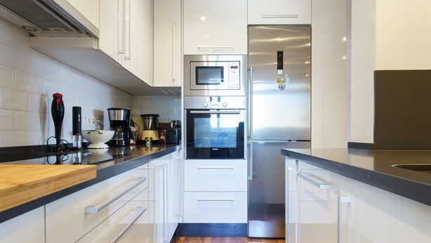 Una cocina moderna con armarios blancos, horno empotrado, microondas y refrigerador de acero inoxidable.