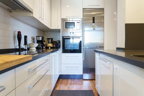 Een moderne keuken met witte kasten, een ingebouwde oven, een magnetron en een roestvrijstalen koelkast.