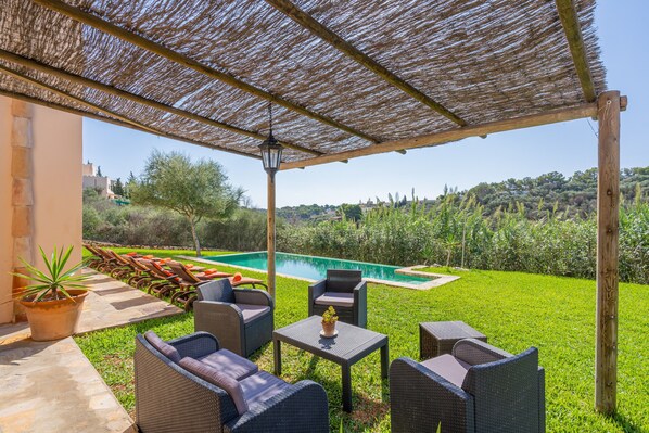A covered outdoor seating area with wicker furniture and a view of a swimming pool.