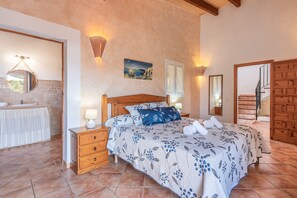 A bedroom with a bed, wooden nightstands, a dresser, a bathroom with a sink and mirror, and a staircase leading to another level.