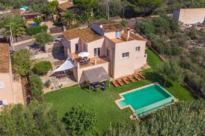 A two-story house with a swimming pool, a patio with outdoor furniture, and a garden.
