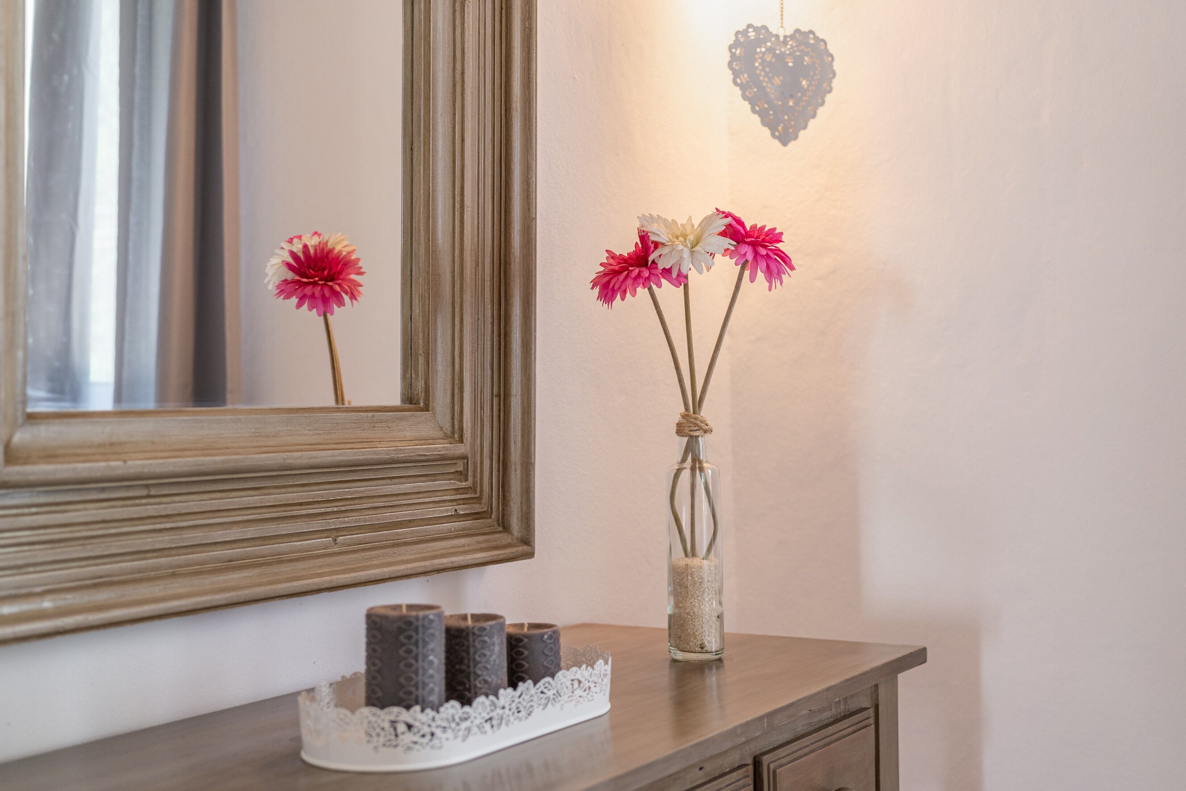 En spegel, en vas med blommor och ljus på en byrå i trä.
