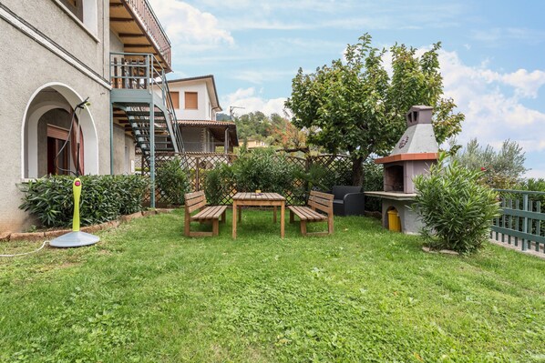Un patio con una mesa y sillas, un pequeño horno de ladrillo y una escalera que lleva a un balcón.