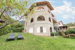 A two-story building with a sloped roof, multiple arched windows, and a balcony. - Apartment Oleandro Casa Demonti with Mountain View, Pool, Terrace & Wi-Fi (Tignale)