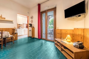 A room with a wooden floor, a dining table with chairs, a TV mounted on the wall, and a sliding glass door leading outside. - Apartment Oleandro Casa Demonti with Mountain View, Pool, Terrace & Wi-Fi (Tignale)