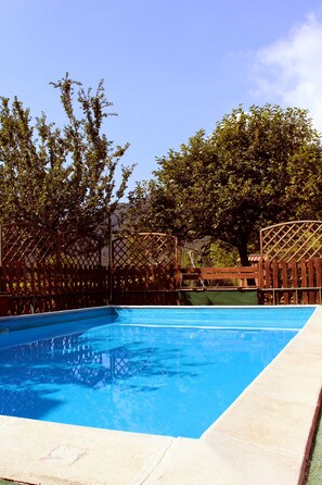 Una piscina rectangular con superficie azul cristalina, rodeada por una valla de madera y árboles.
