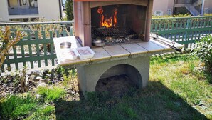 Un barbecue extérieur avec des flammes, un plateau rempli de nourriture et un banc.
