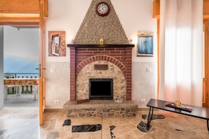 Une cheminée en pierre avec une horloge, une table avec un vase et une vue sur l’extérieur.