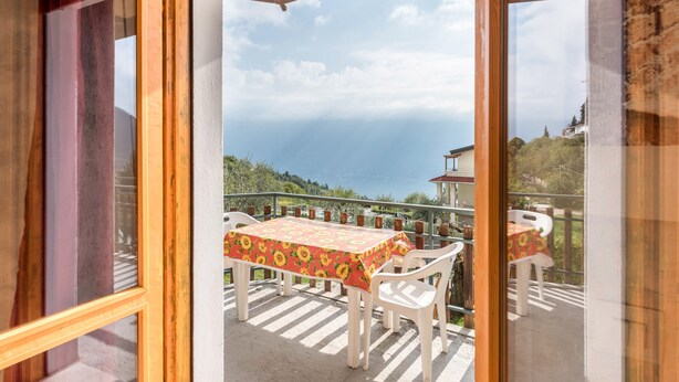A balcony with a table and chairs, a view of the sea, and a building in the background.