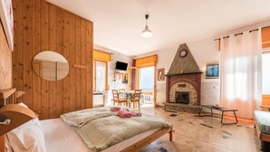 A bedroom with a wooden bed, a fireplace, a dining area with chairs, and a TV.