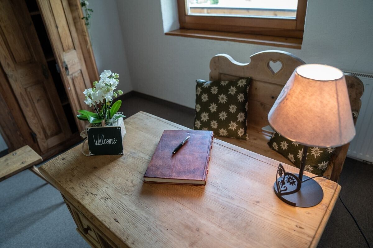 Una mesa de madera con un libro, un cartel que dice 'Welcome', una lámpara y un cojín floral.