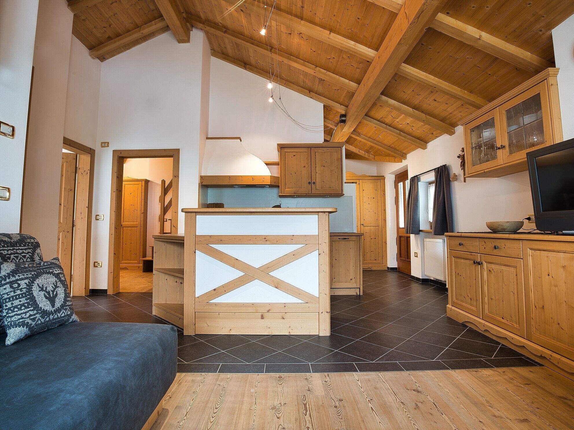 A modern kitchen with wooden cabinets, a central island, and a dining area with a sofa.