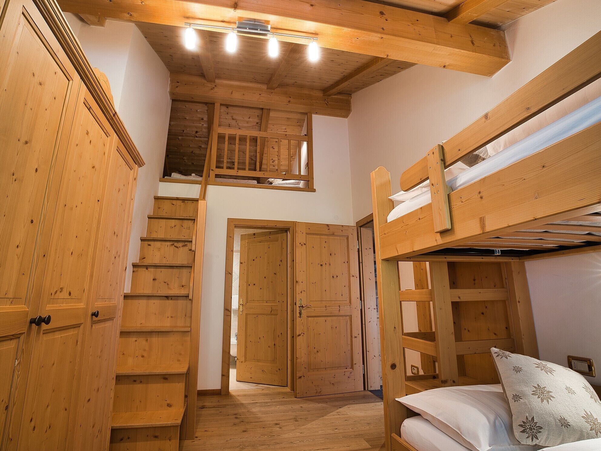 A wooden interior with bunk beds, a staircase, and a door leading to another room.
