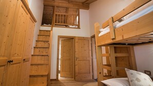 Een houten interieur met stapelbedden, een trap en een deur naar een andere kamer.