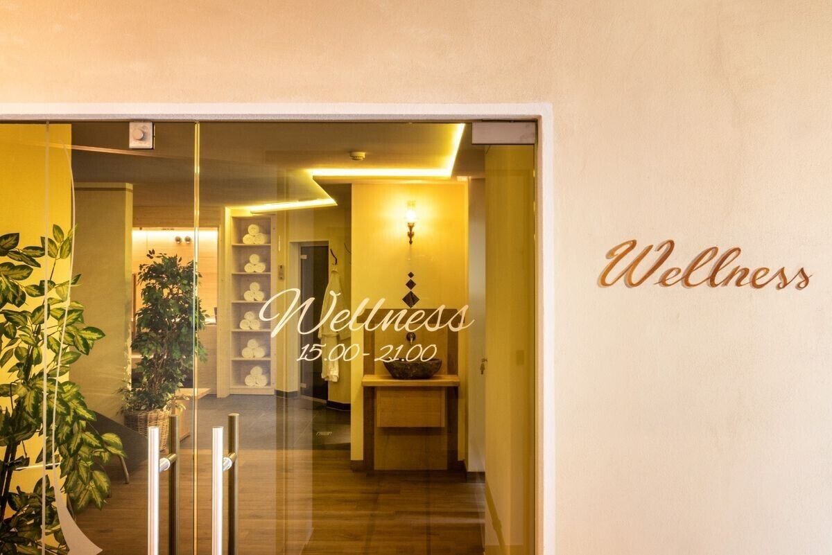A wellness center interior with a reception area, a reception desk, and a wall with the word 'Wellness' and operating hours.