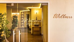 Interieur van een wellnesscentrum, met een receptie, een receptiebalie en een muur waarop 'Wellness' en de openingstijden staan.