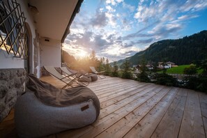 Une terrasse en bois avec deux fauteuils en forme de sac de haricots, un mur en pierre et une vue sur un paysage montagneux.