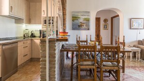 Una cocina con armarios de madera, una mesa de comedor con sillas y un cuadro en la pared.