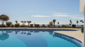 Una piscina azul cristalina con un muelle de madera, rodeada de palmeras y vista al mar.