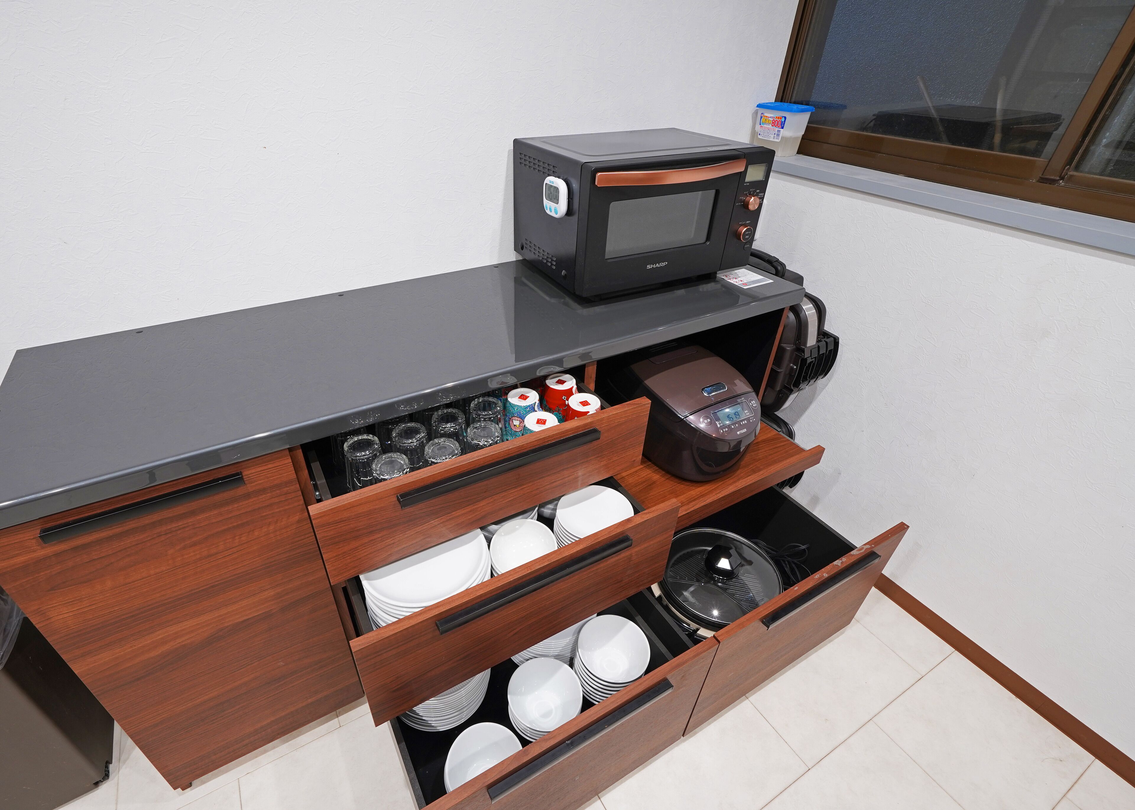 Cozinha compacta com micro-ondas, cafeteira e gaveta com pratos e tigelas empilhados.