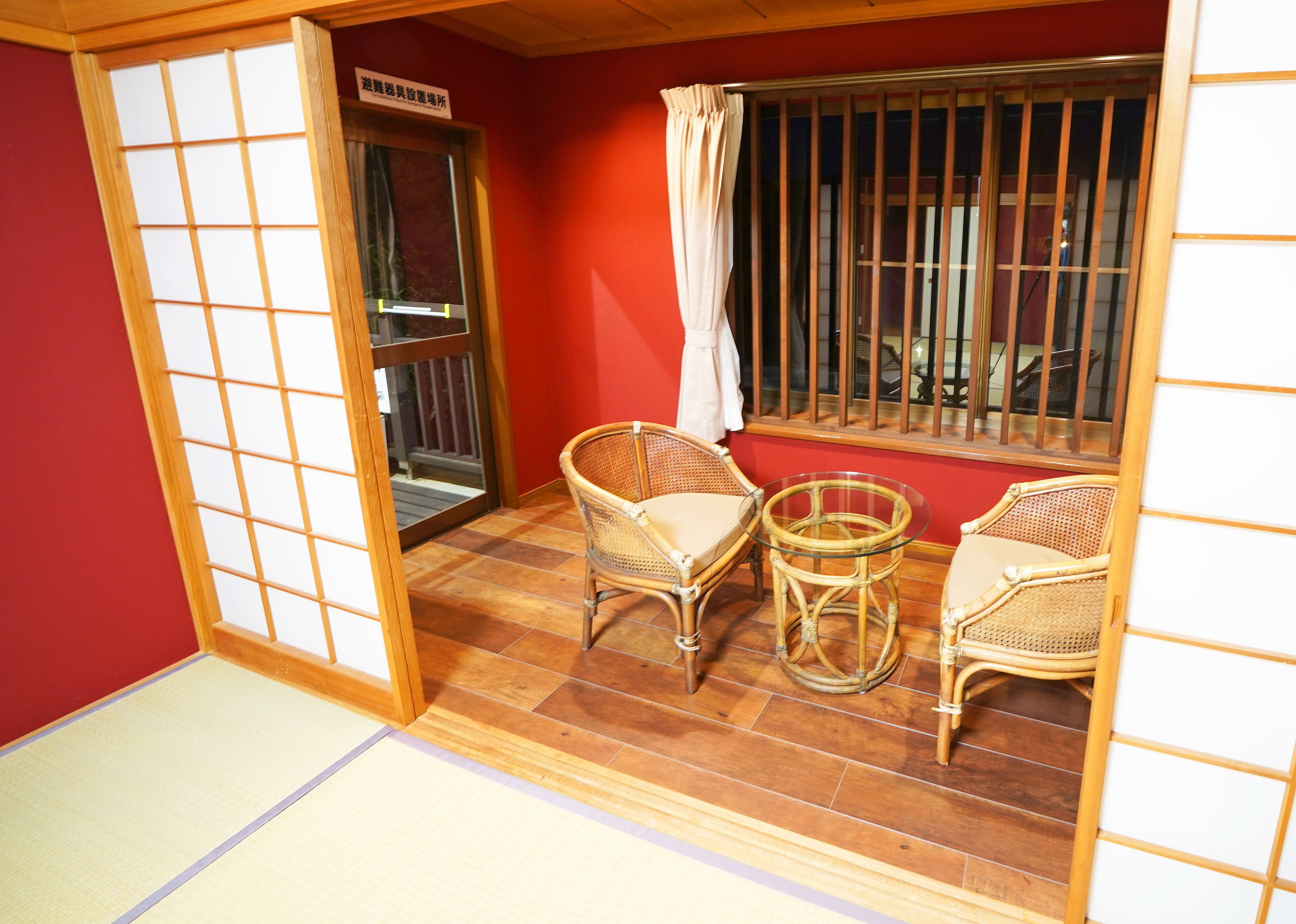 A room with a sliding door, two wicker chairs, a small glass table, and a window with bars.