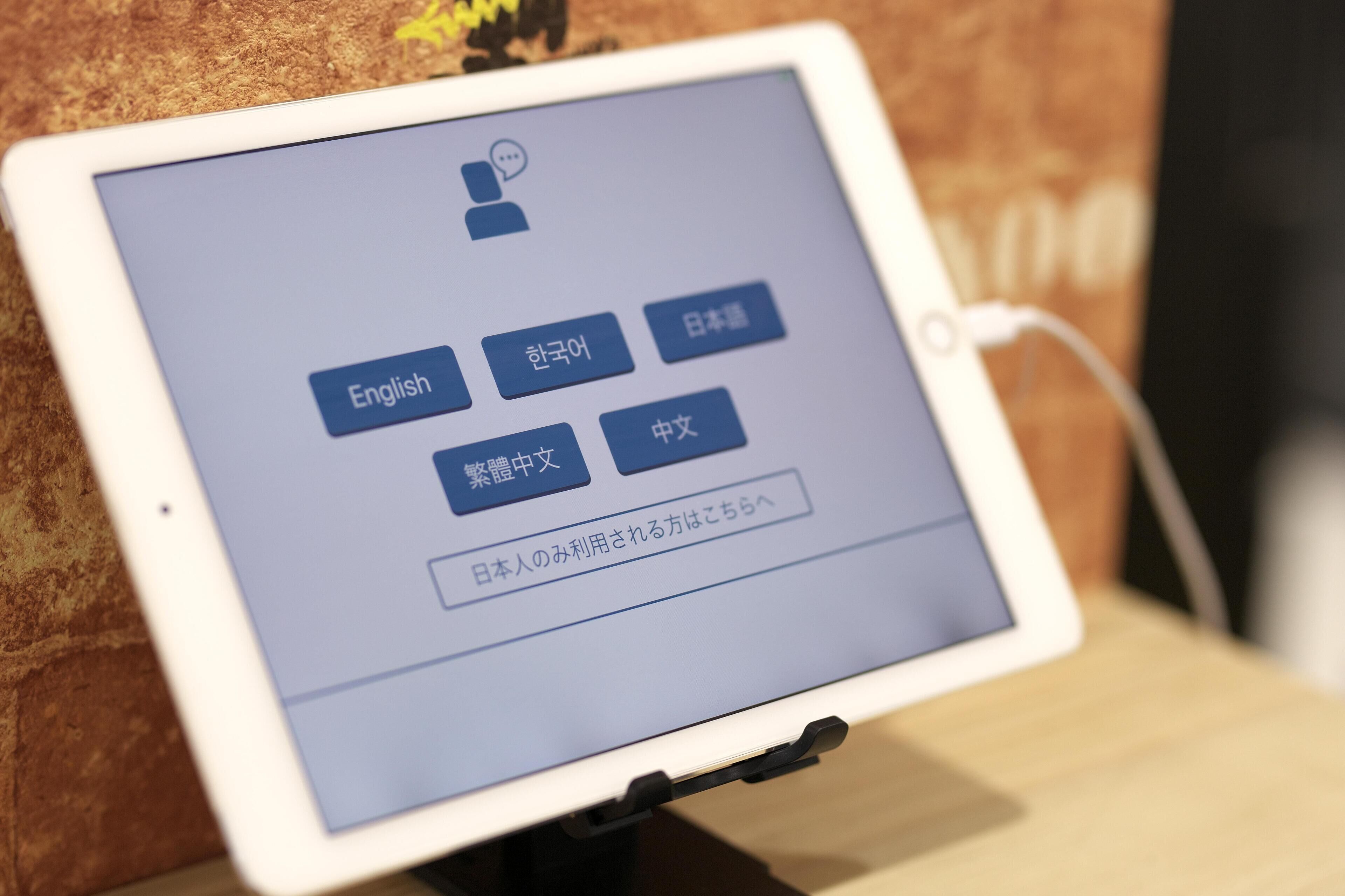 A tablet displaying a language selection interface with options for English, Korean, Japanese, and Chinese.