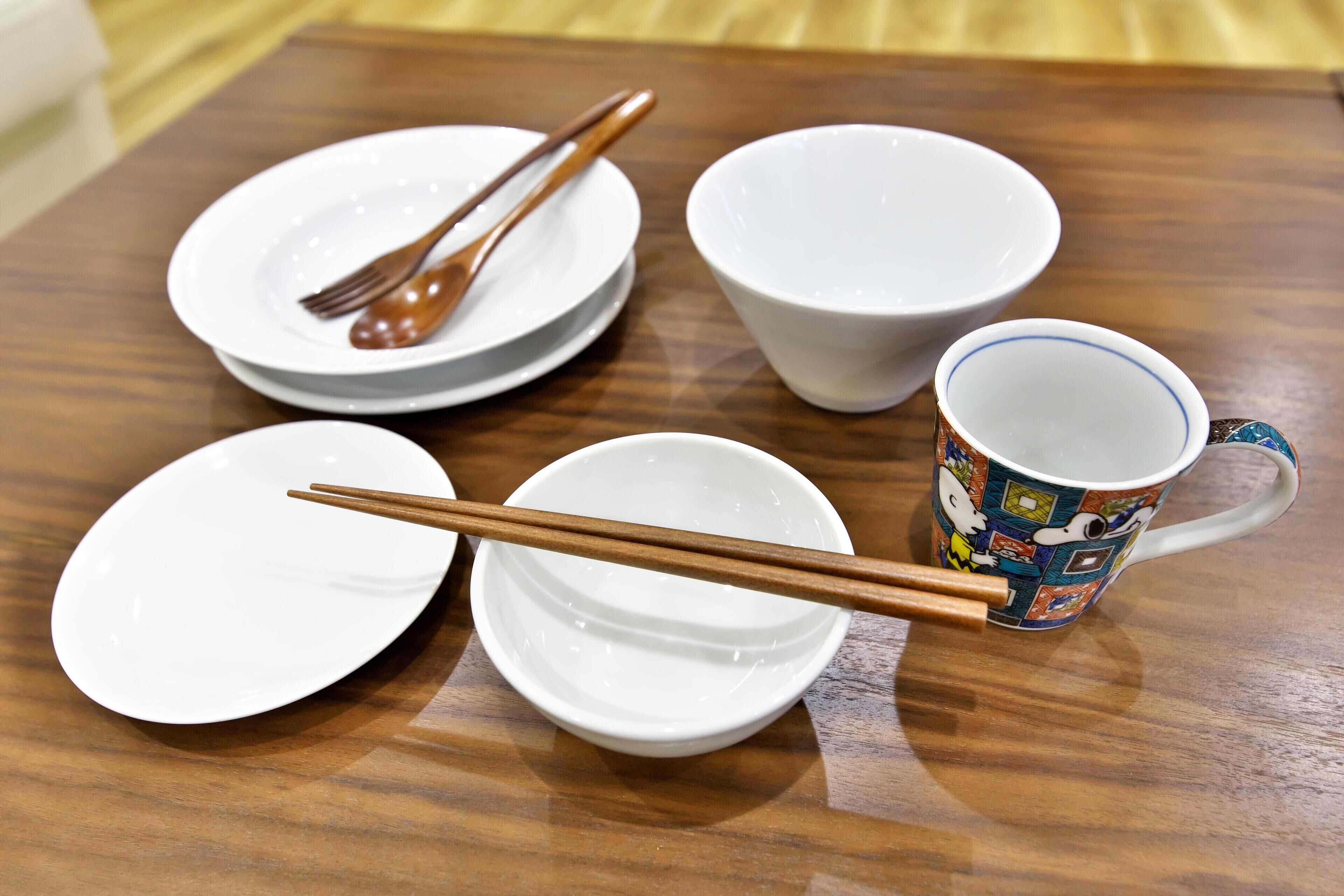 Una mesa de madera con platos blancos, palillos y una taza de colores.