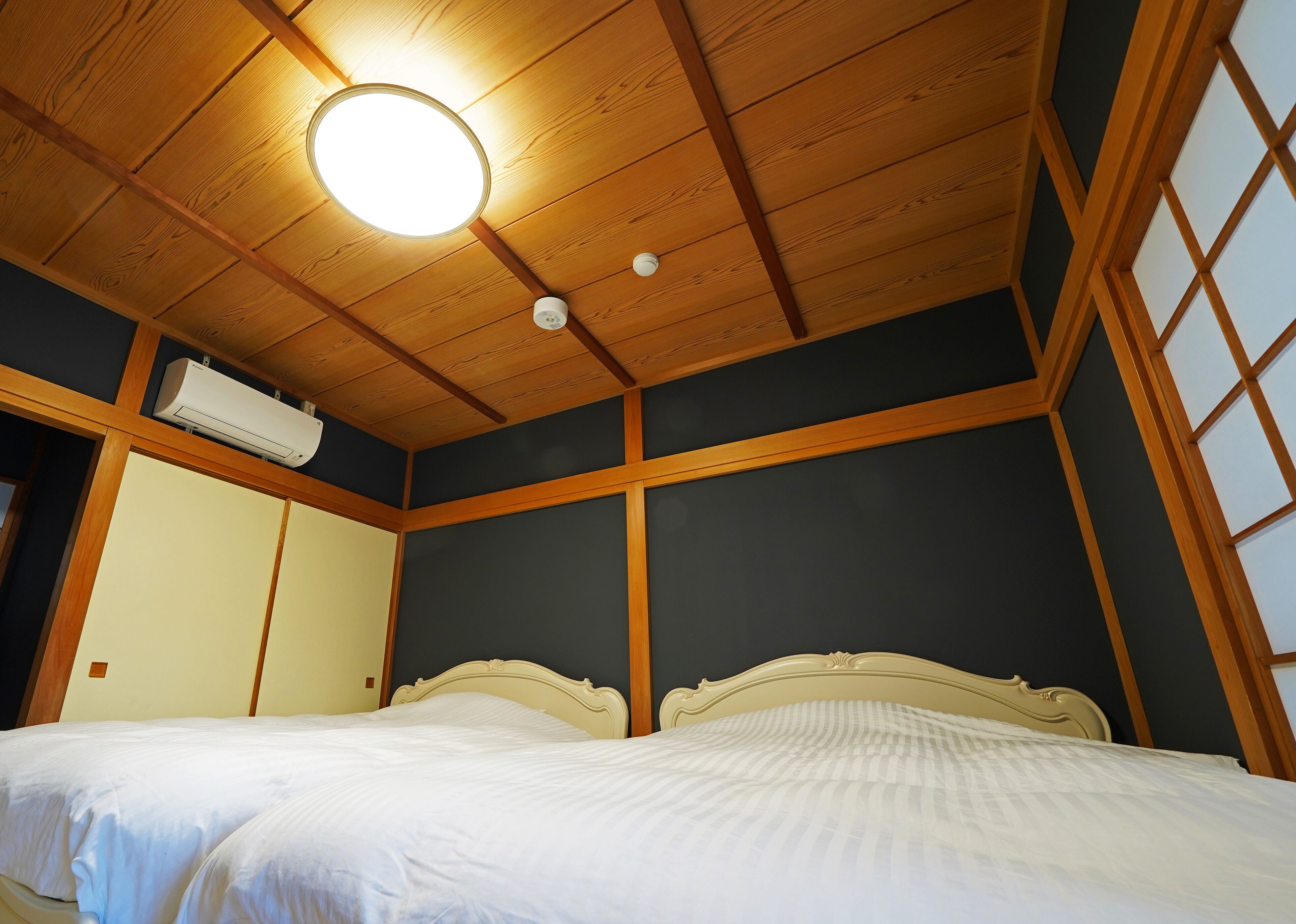 Une pièce avec un plafond en bois, un lit avec une literie blanche et un climatiseur fixé au mur.