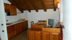 A compact kitchen with wooden cabinets, a dining table, and a television. - Monterosa Residence Hotel (Macugnaga)