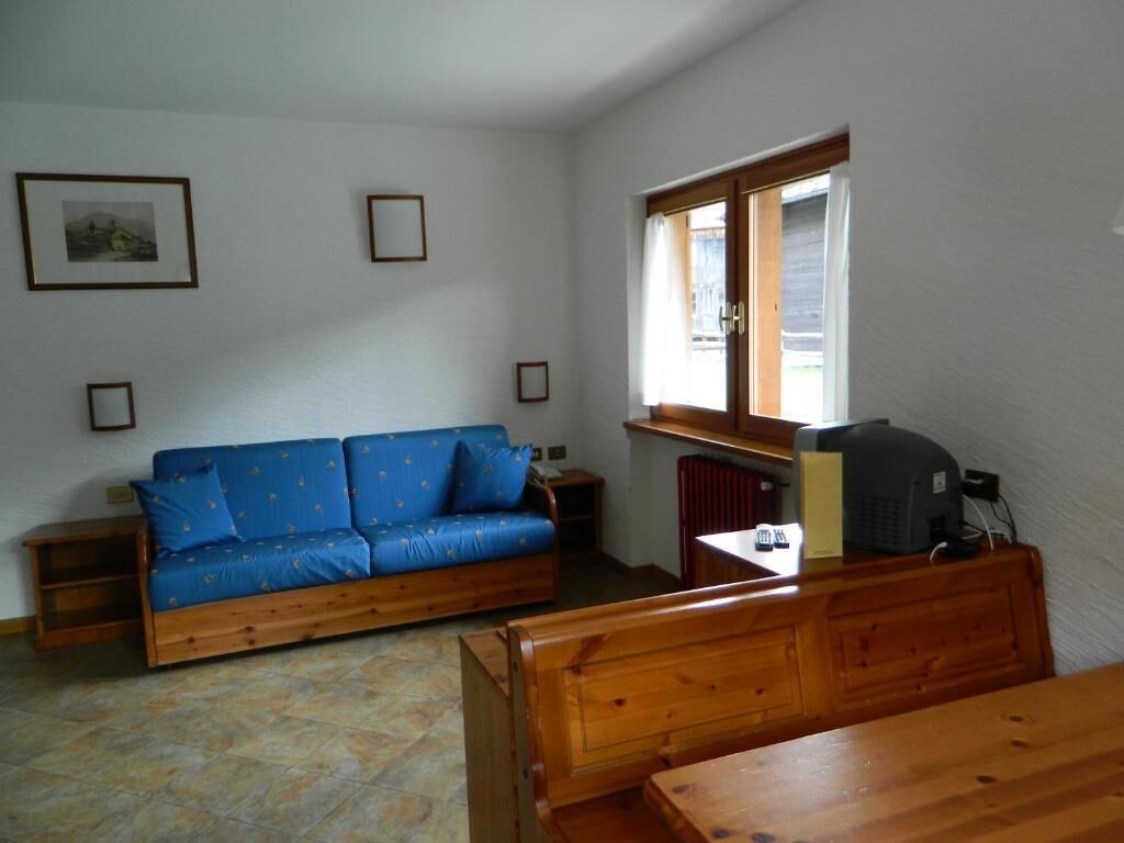 Una habitación con un sofá azul, un banco de madera, un radiador y una ventana con cortinas.