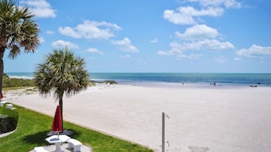 Ein Strand mit einer Palme, einem roten Sonnenschirm und einem weißen Tisch mit Bänken.