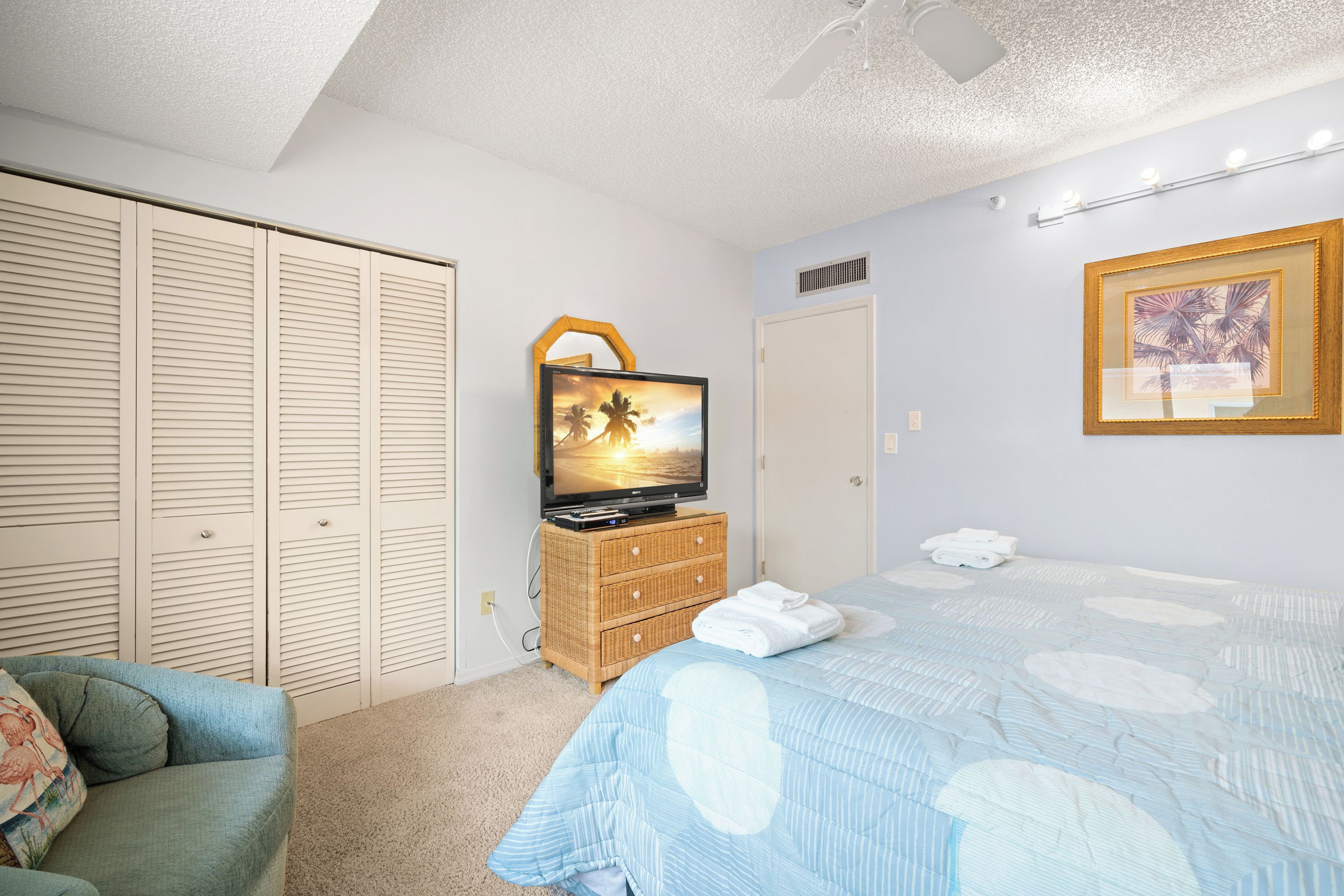 A bedroom with a bed, a television on a dresser, a closet, and a framed picture on the wall.