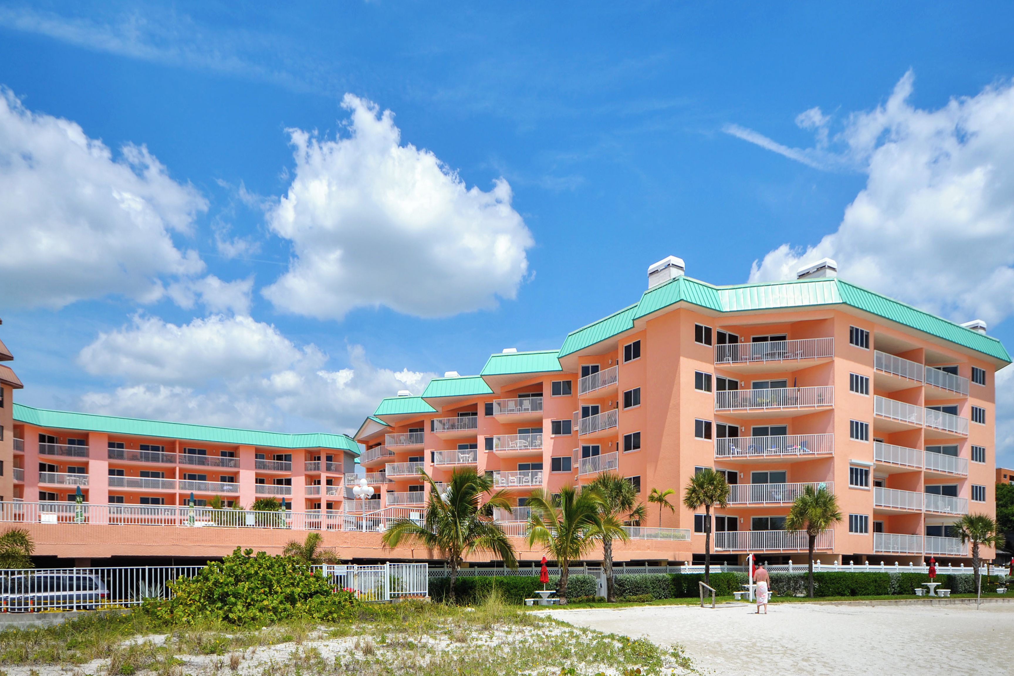 A multi-story hotel with balconies, a beach view, and palm trees.