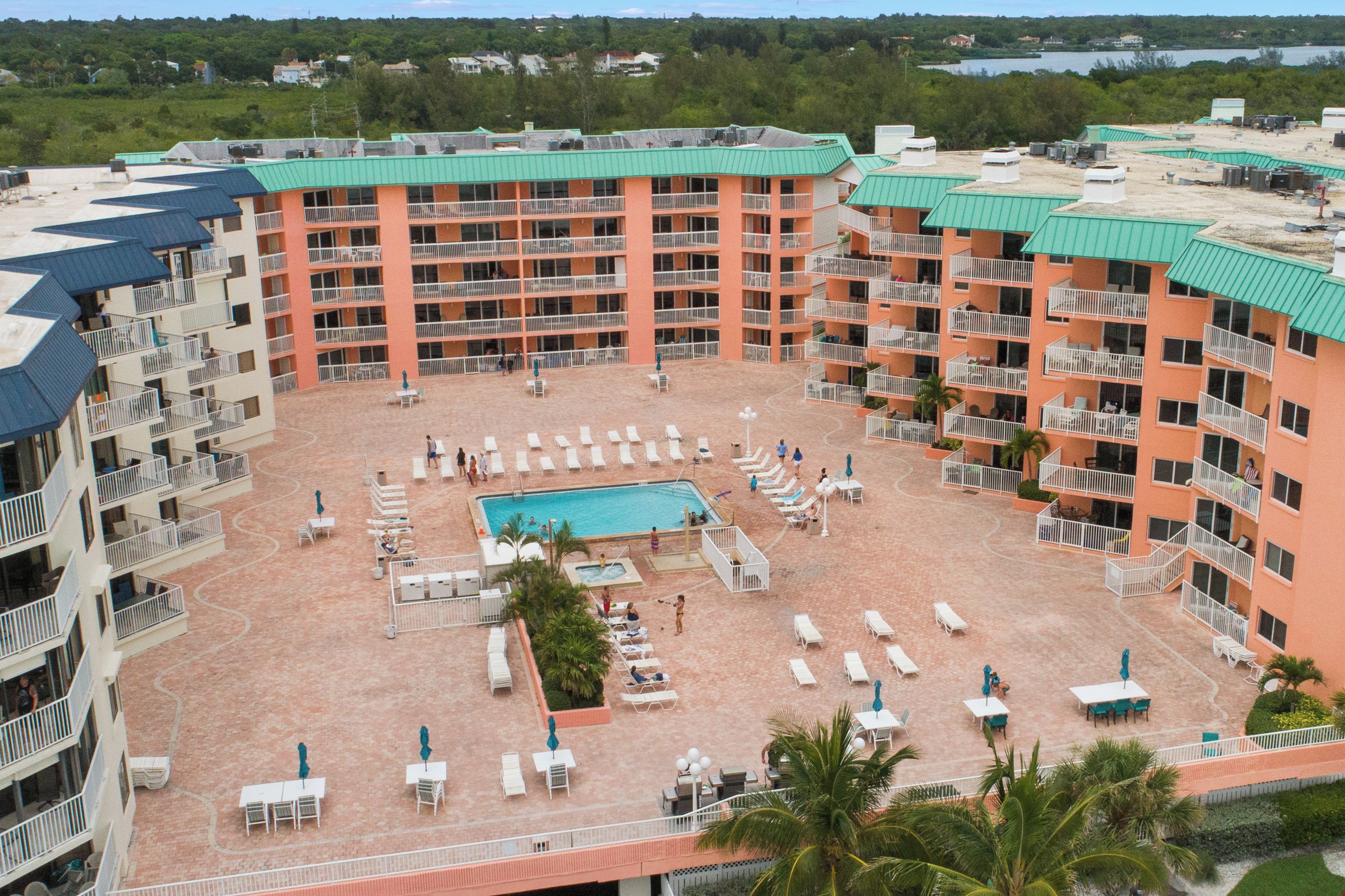 A multi-story hotel with a central pool surrounded by sun loungers and tables, balconies on each floor, and a view of a lake in the background.