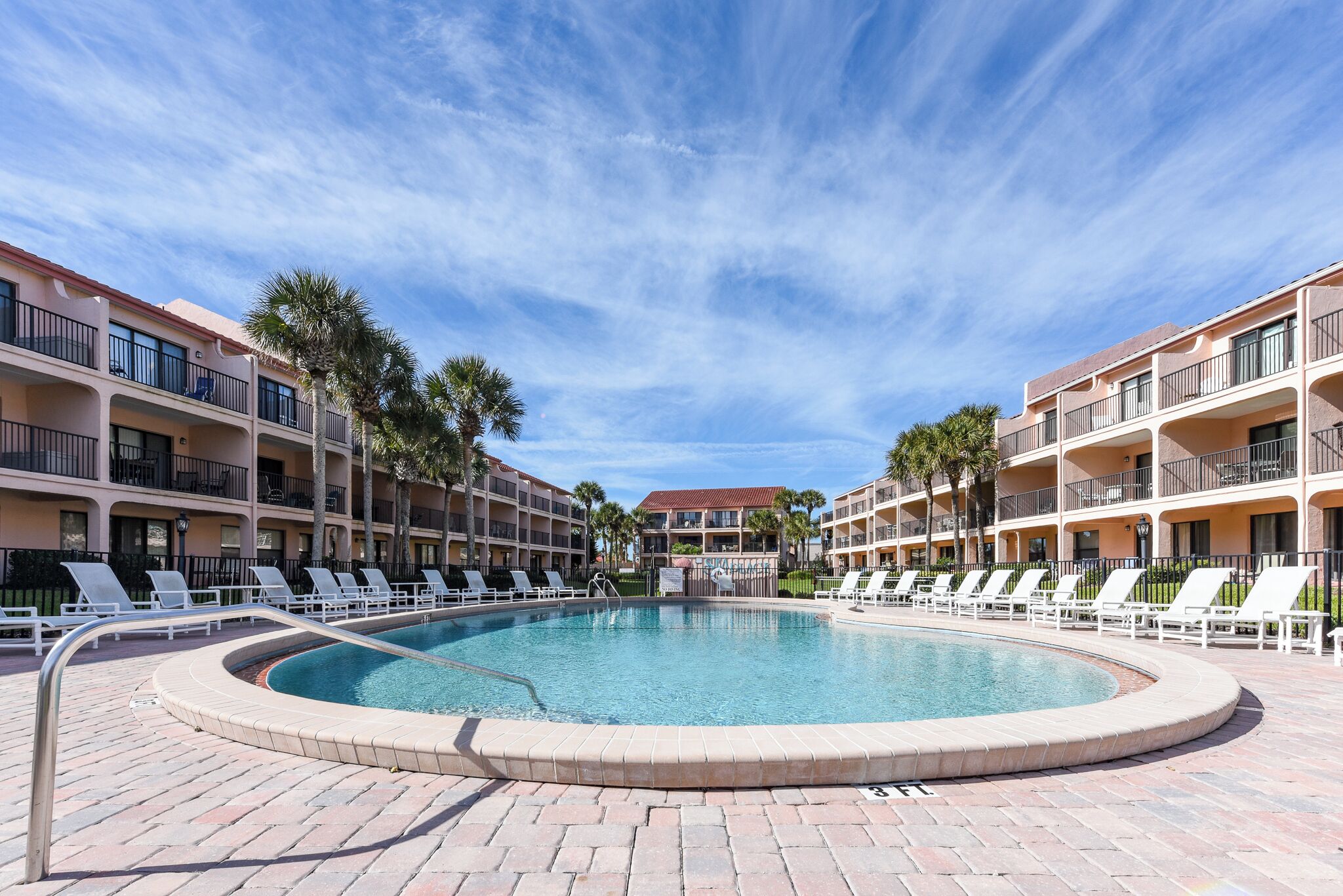A pool area with lounge chairs and a circular pool, surrounded by multi-story buildings with balconies.