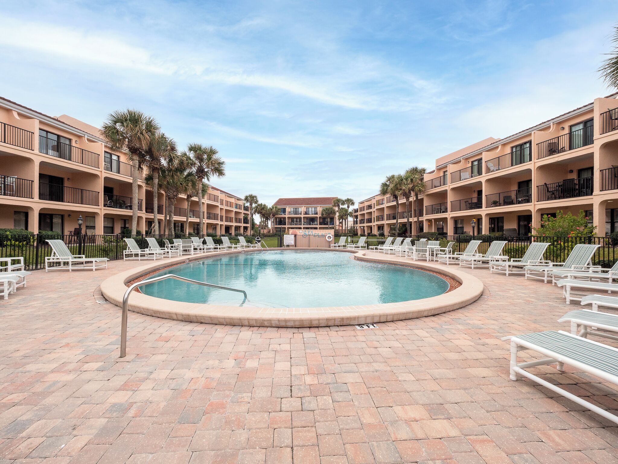 A pool area with lounge chairs and a circular pool, surrounded by multi-story buildings with balconies.