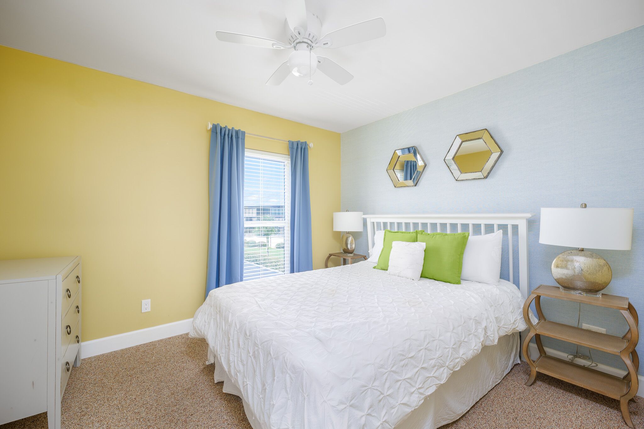 A bedroom with a bed, a nightstand, a dresser, a ceiling fan, and a window with curtains.