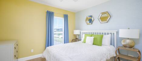 A bedroom with a bed, a nightstand, a dresser, a ceiling fan, and a window with curtains.