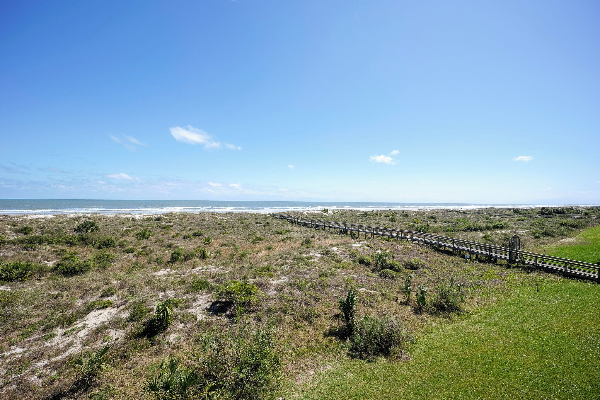 A coastal landscape with a wooden boardwalk leading to a grassy area.