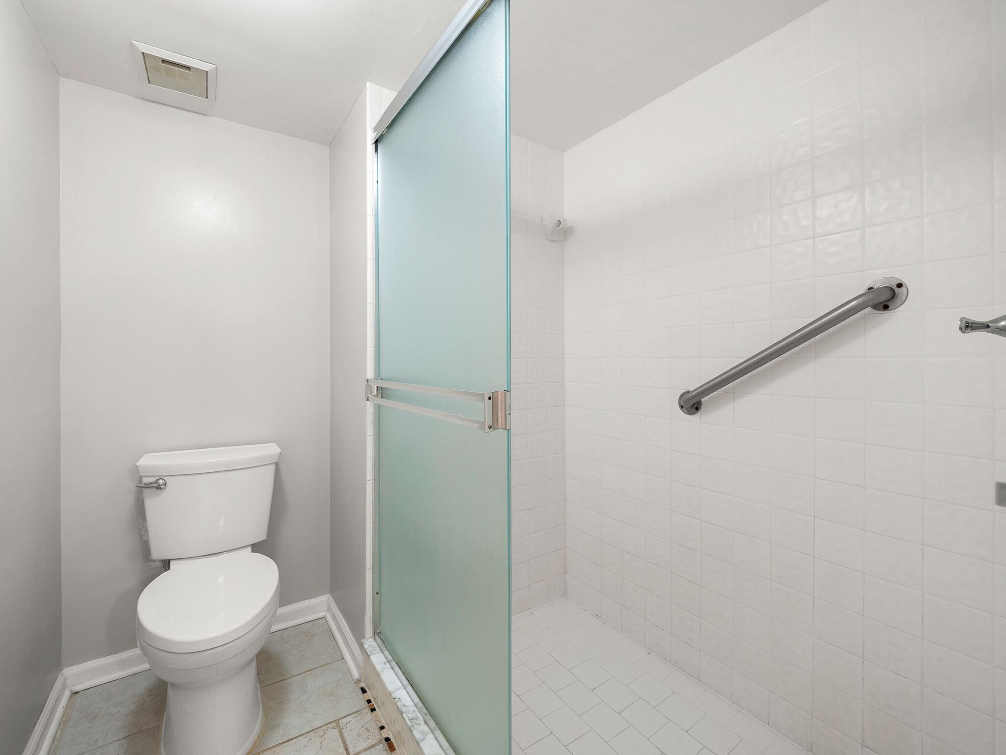 Ein Badezimmer mit Toilette, einer Dusche inklusive Haltegriff und einer Glastür.