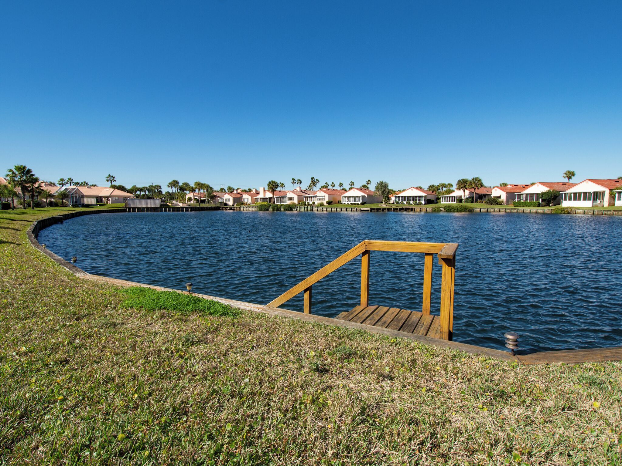 A waterfront property with a wooden deck, a curved water body, and a row of houses with red roofs.