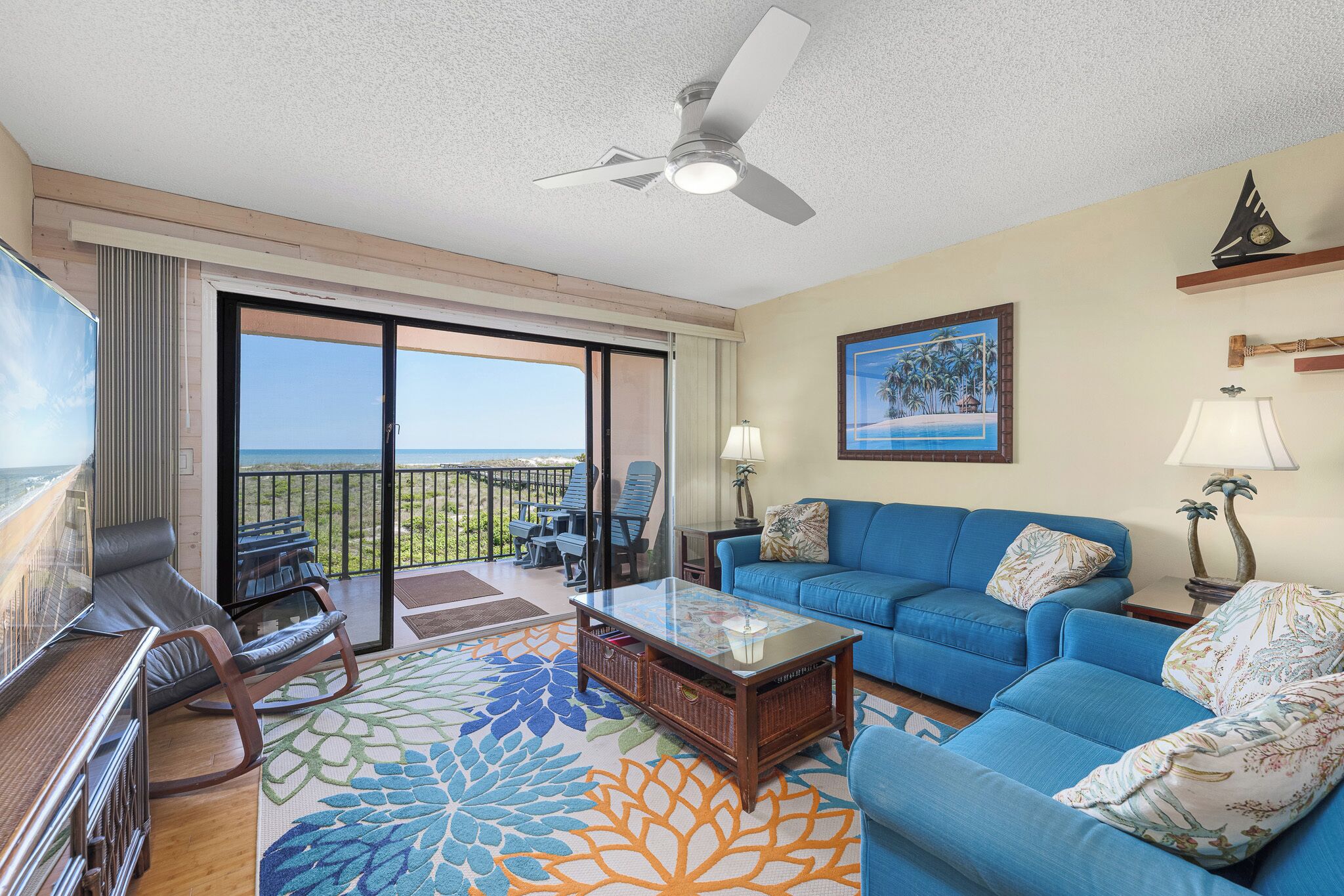 A spacious living room with a balcony, a blue sofa, a coffee table, and a TV.