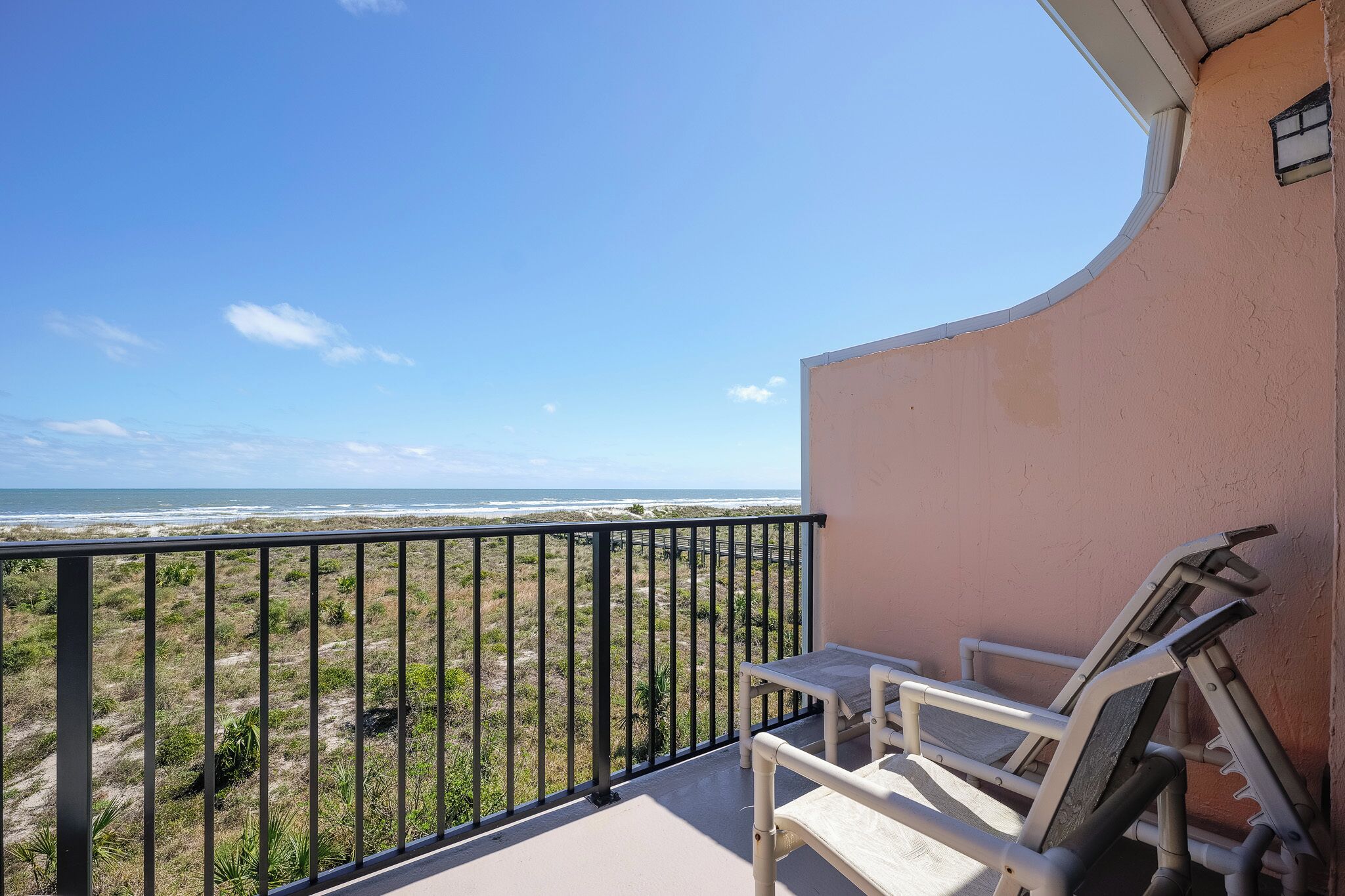 A balcony with a view of the beach and ocean, a table, and two chairs.