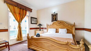 A neatly made bed with a wooden headboard, a bedside table with a lamp, and a window with curtains. - OYO 120 Concord International Hotel (Manama)
