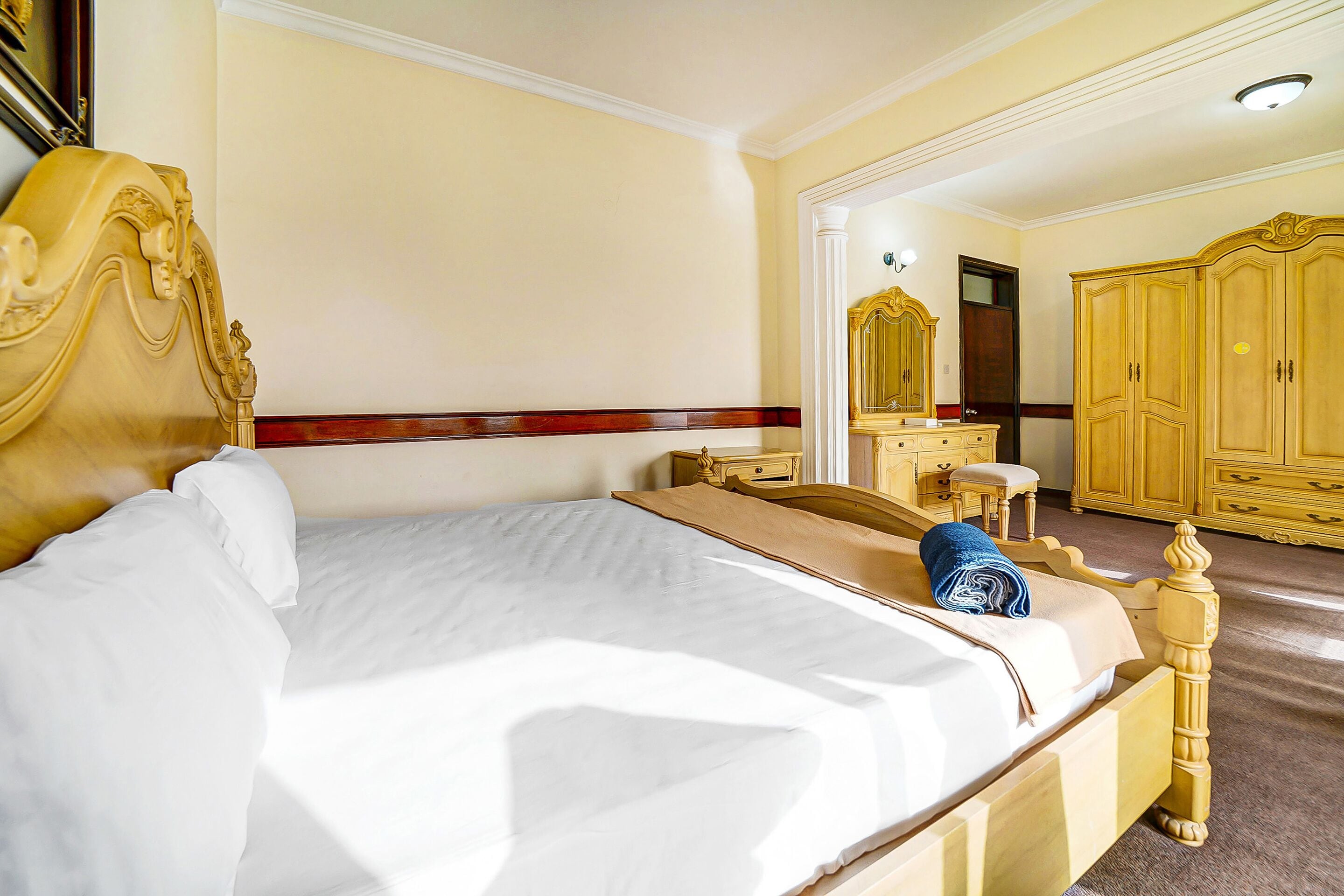 Ein Hotelzimmer mit einem großen Bett, einem Holzkopfende, einem Schminktisch und einem Kleiderschrank.
